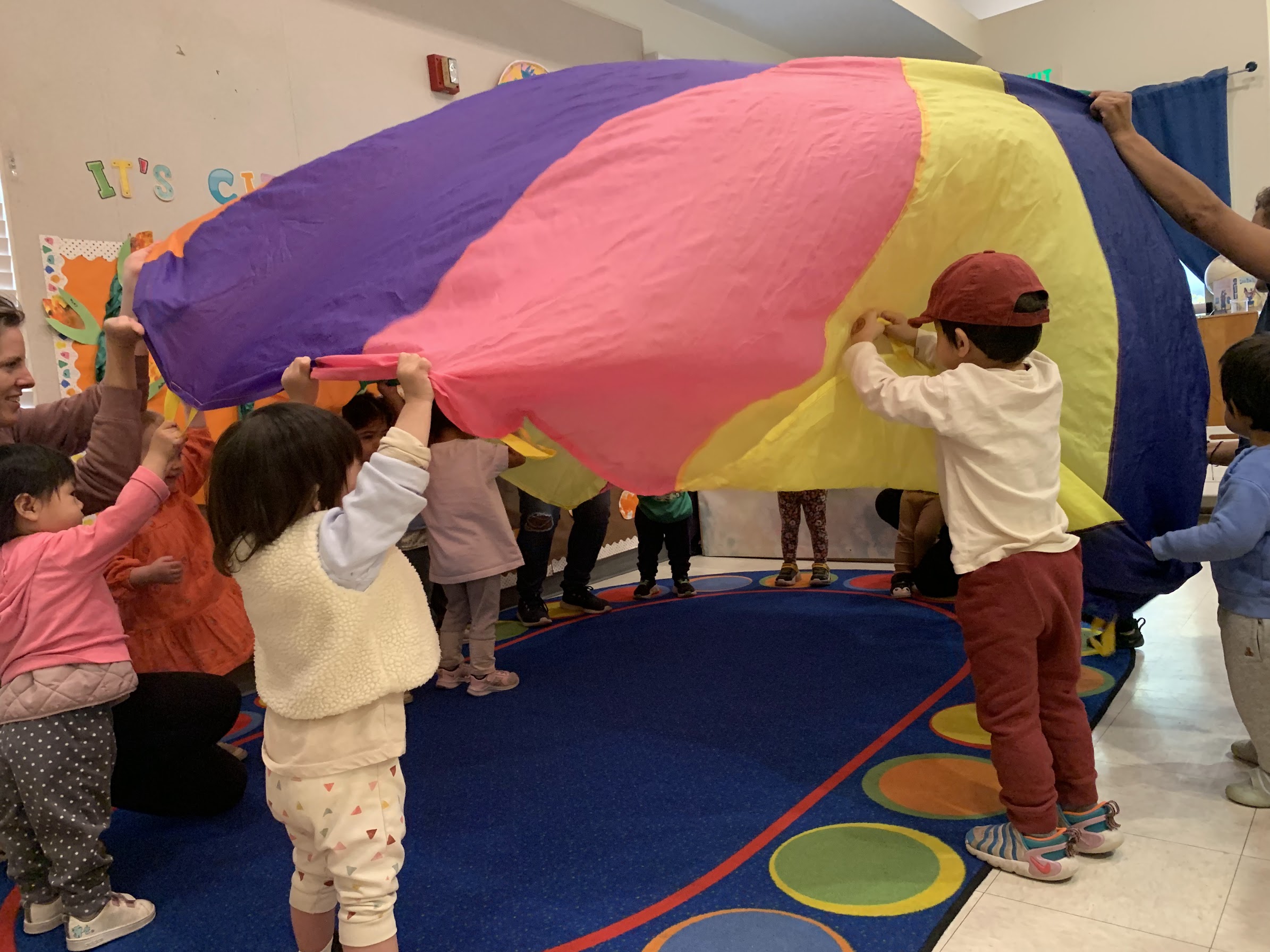 Children, teachers, and parents playing with a colorful parachute at UPNS
